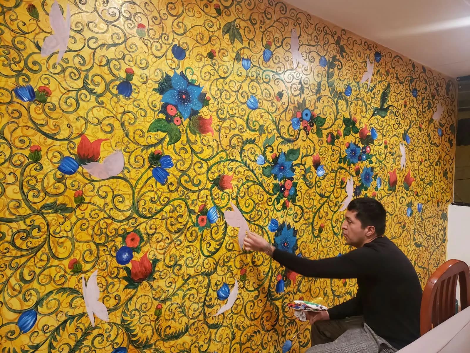 Joan Alfaro pintando un gran mural floral dorado en el hotel