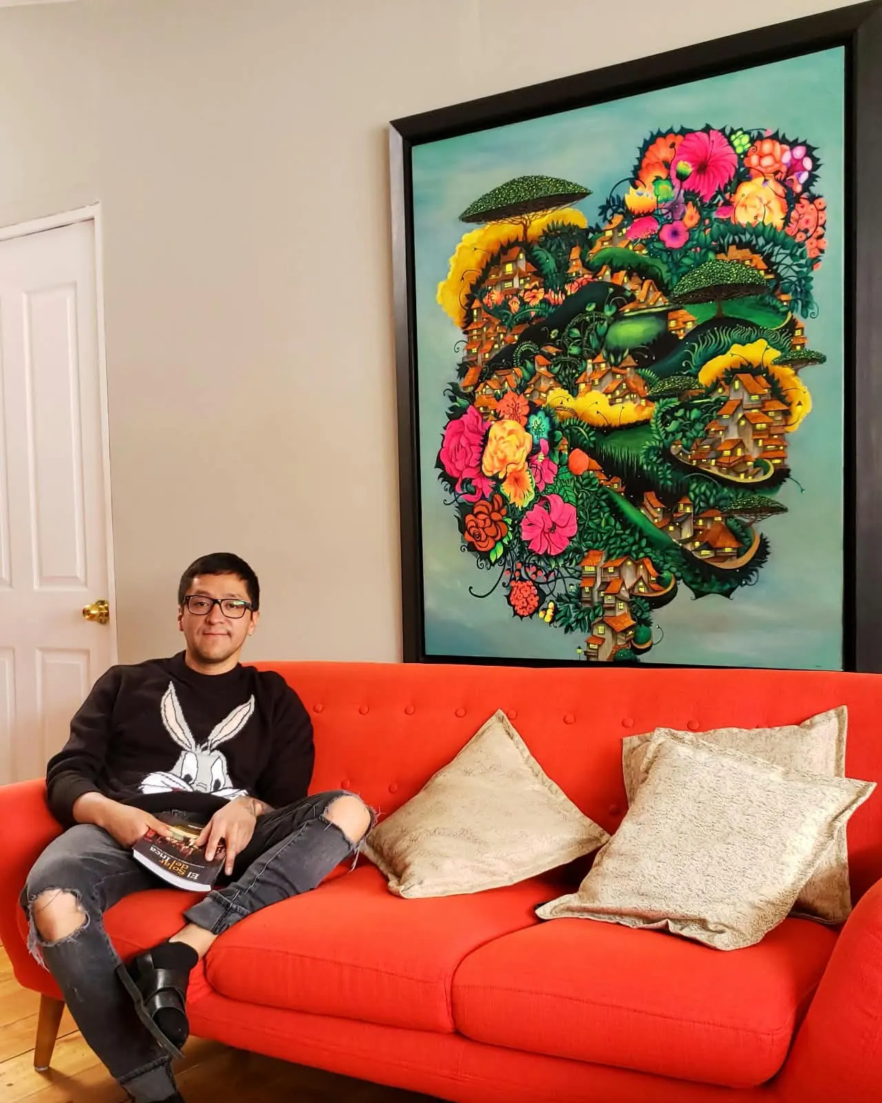 Joan Alfaro junto a una pintura de paisaje fantástico y flores
