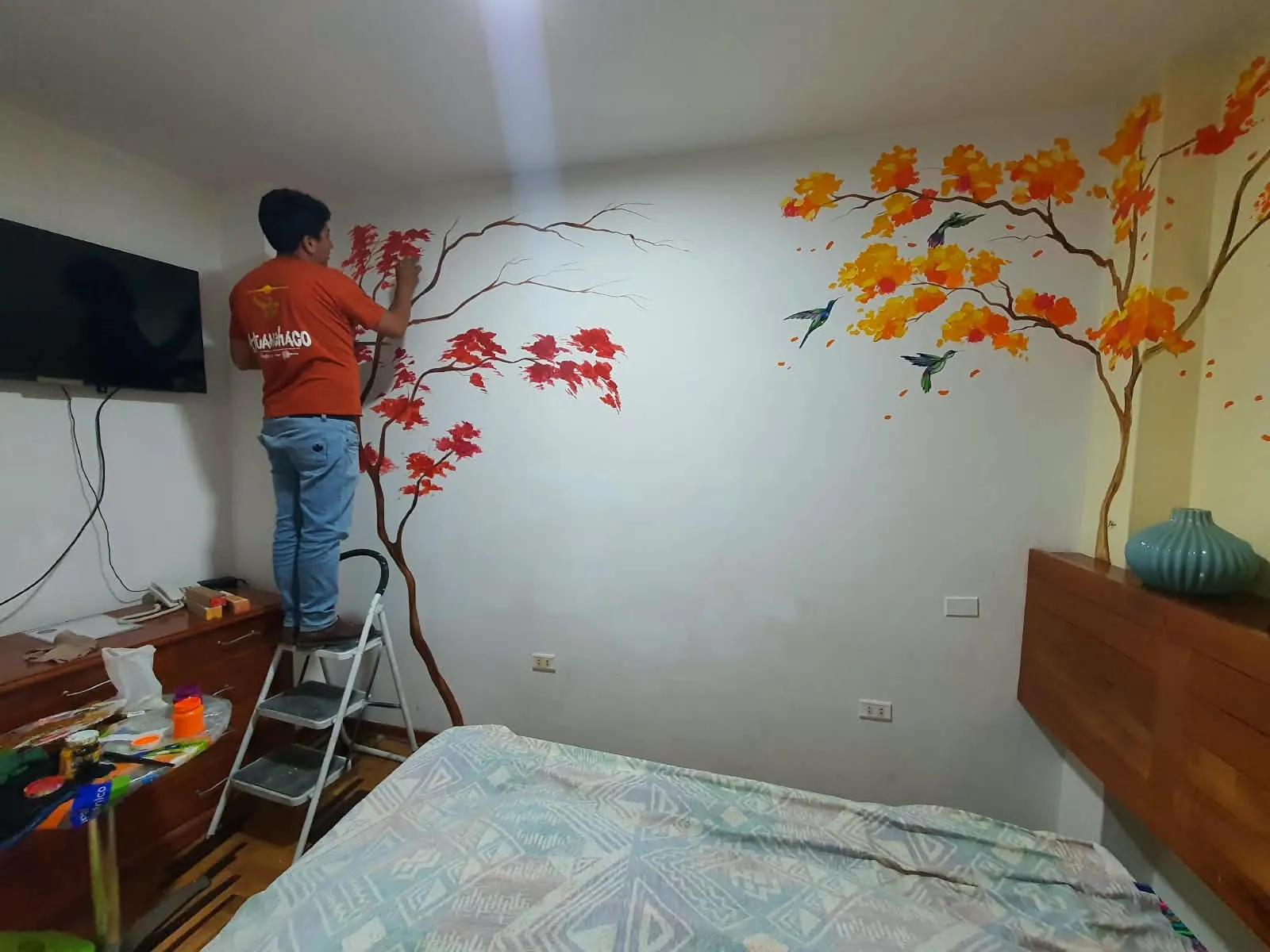 Kadu Izquierdo pintando un mural de ramas y colibríes en una habitación del hotel